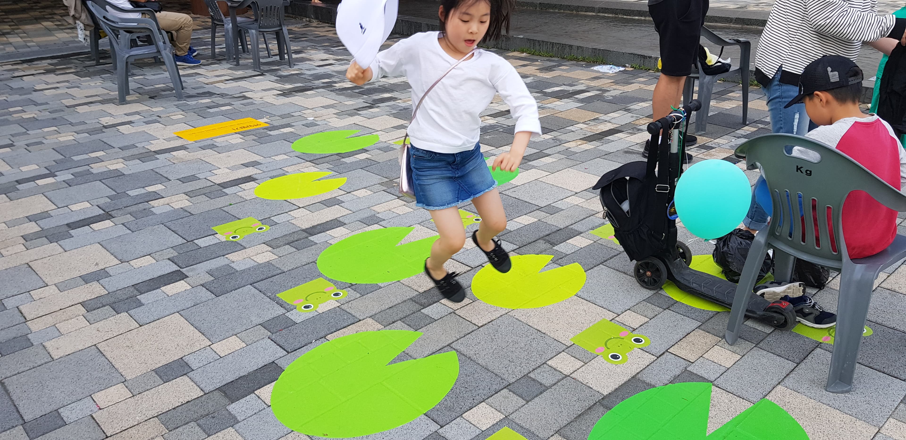 광장 바닥에 부착된 연잎 그래픽 위를 아이가 뛰어 건너는 모습
